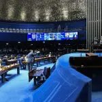 Imagem do plenário do Senado Federal, com painel de votação e carpete azul
