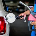 Funcionário de posto segura bomba de combustível enquanto fecha o tanque de um carro