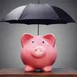 Cofrinho em forma de porco cor-de-rosa protegido por um guarda-chuva