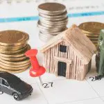 Moedas, carro e casa representando compra sobre um calendário. Foto: Adobe Stock