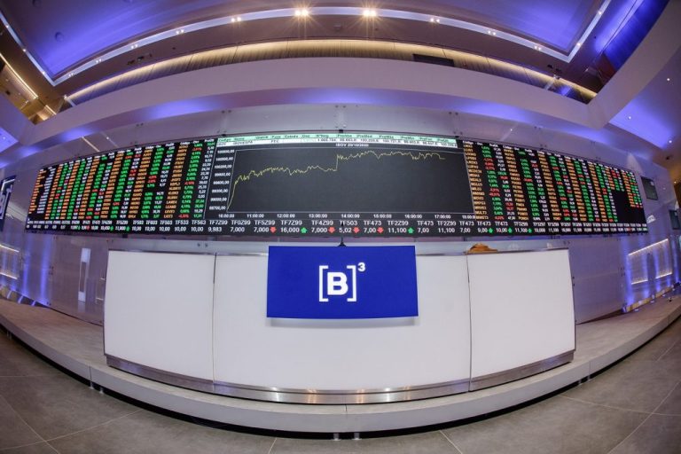 Balcão da b3 em frente a uma tela com gráficos