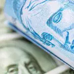 Rolo de cédulas de Real cruzada sobre notas de Dólar