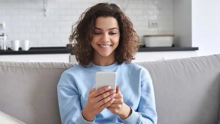 Mulher sentada no sofá segurando um celular. Foto: Adobe Stock