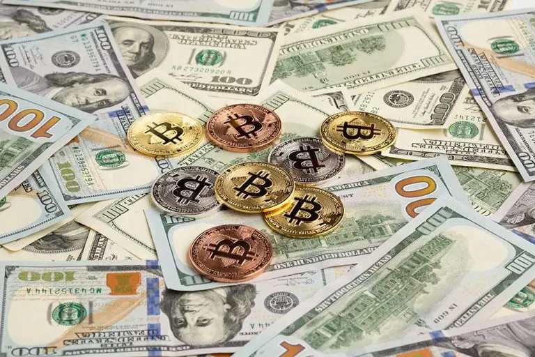 Bitcoins em cima de dinheiro de papel. Foto: Pexels