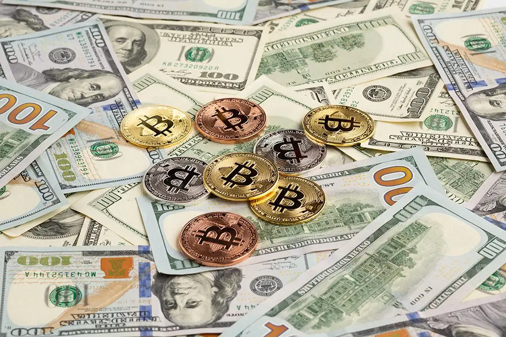 Bitcoins em cima de dinheiro de papel. Foto: Pexels