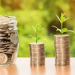 Pote de vidro com moedas seguido de moedas em pilhas crescentes. Foto: Pixabay