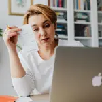 Mulher na frente de notebook com boleto na mão. Foto: Pexels