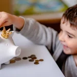 Criança colocando moedas em cofre de porquinho. Foto: Pixabay