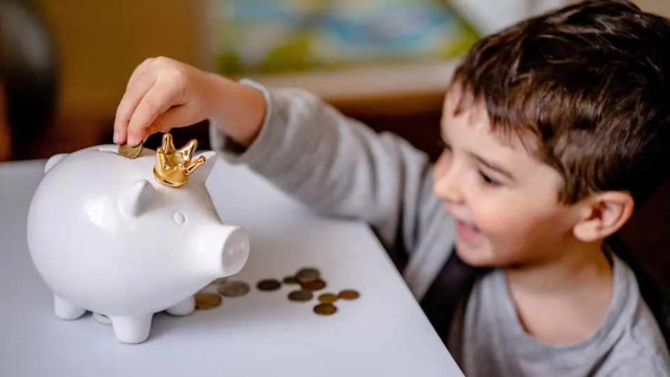 Criança colocando moedas em cofre de porquinho. Foto: Pixabay
