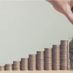 Fileira de moedas em tamanho crescente até um pote cheio de moedas. Foto: Adobe Stock