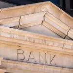 Fachada de pedra com a palavra Banco gravada. Foto: Adobe Stock